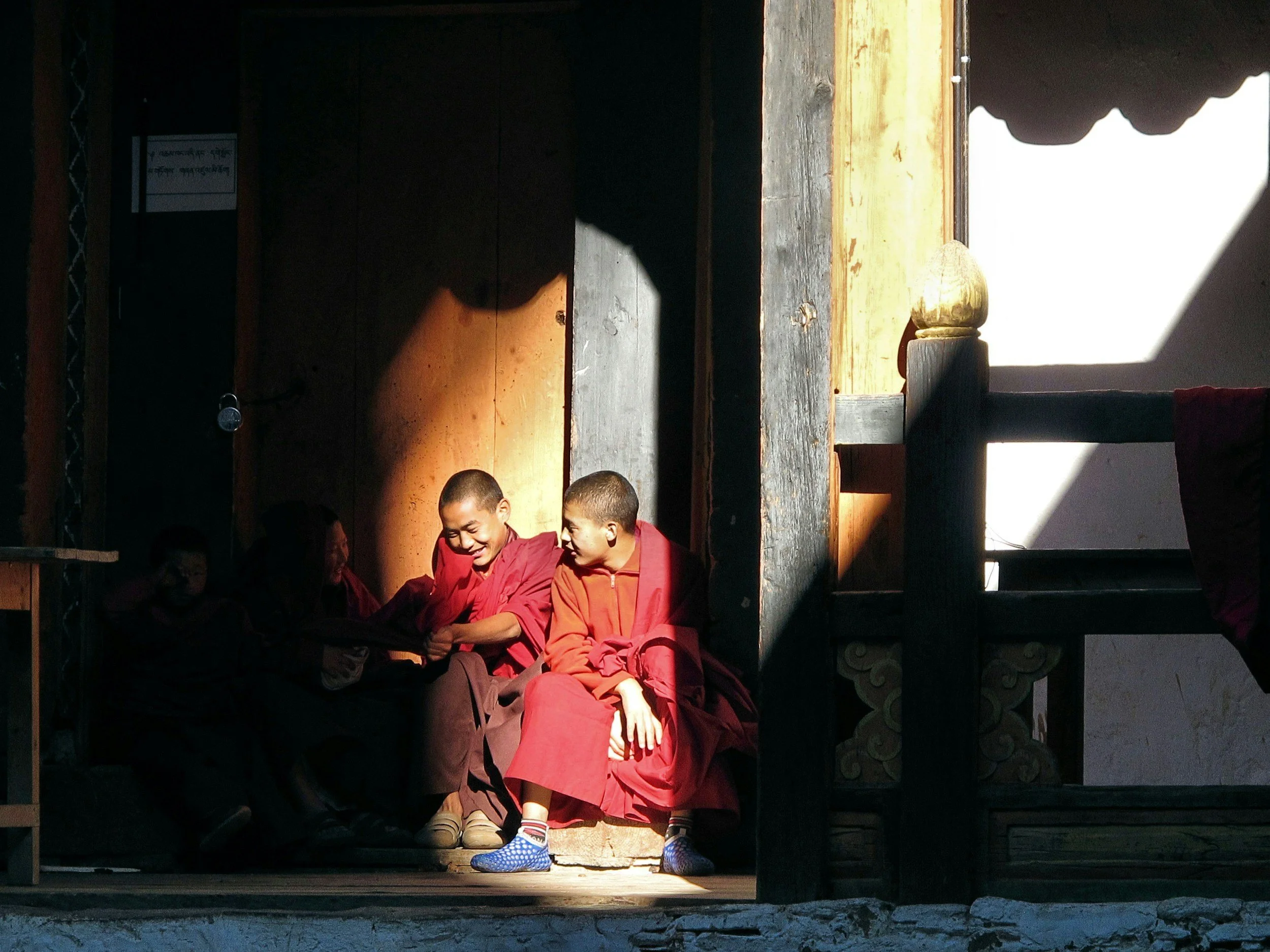 Young monks in crimson robes sharing a quiet moment in warm light, Bhutan